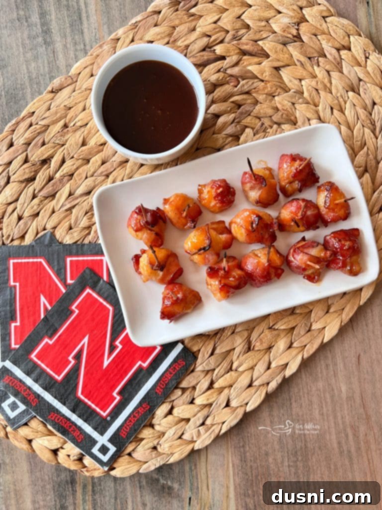A close-up of a single bacon-wrapped water chestnut, perfectly glazed with BBQ sauce and skewered with a toothpick.