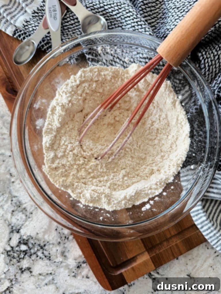A hand whisking together flour, baking powder, and salt in a mixing bowl to create homemade self-rising flour.