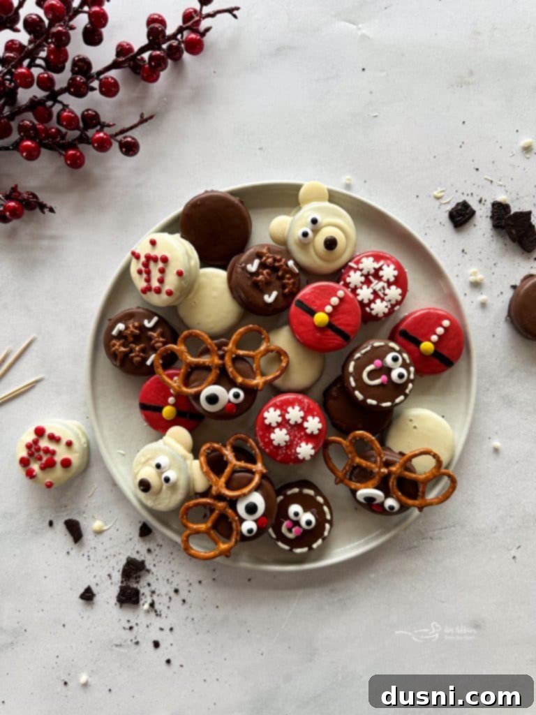 Assorted festive chocolate-dipped Christmas Oreos, including Santa, reindeer, and polar bear designs, arranged artfully on a white plate with evergreen sprigs.
