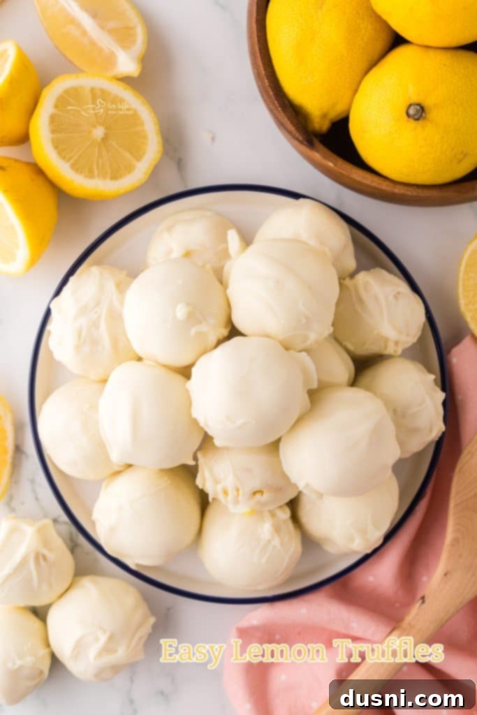 A stack of two easy lemon truffles, with a few fresh lemon slices in the background.