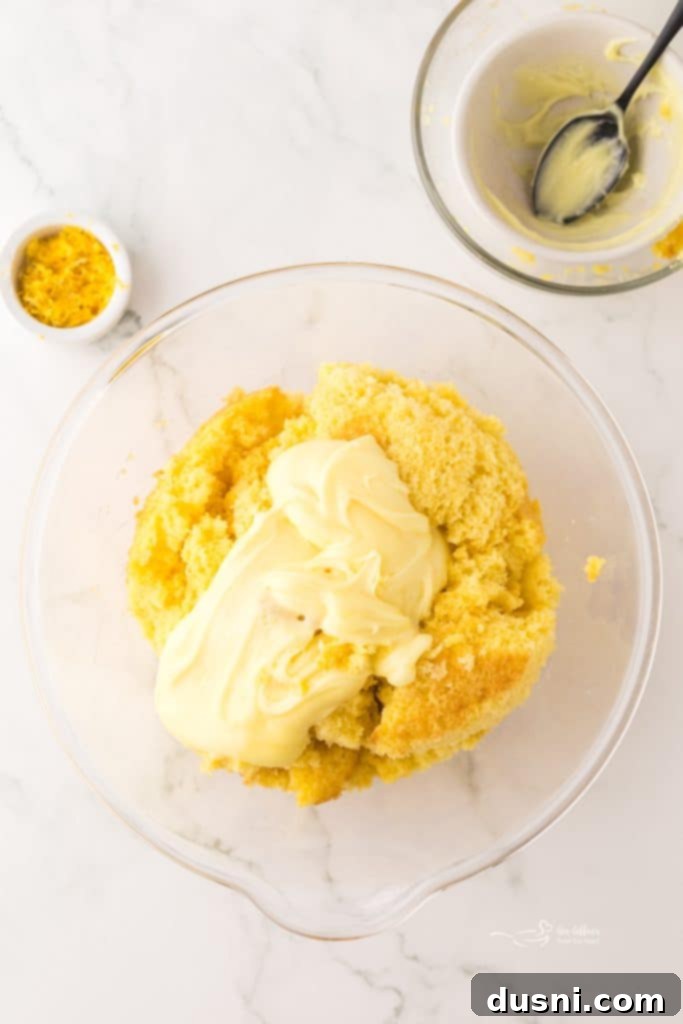 Electric hand mixer combining lemon cake crumbs and frosting in a bowl.