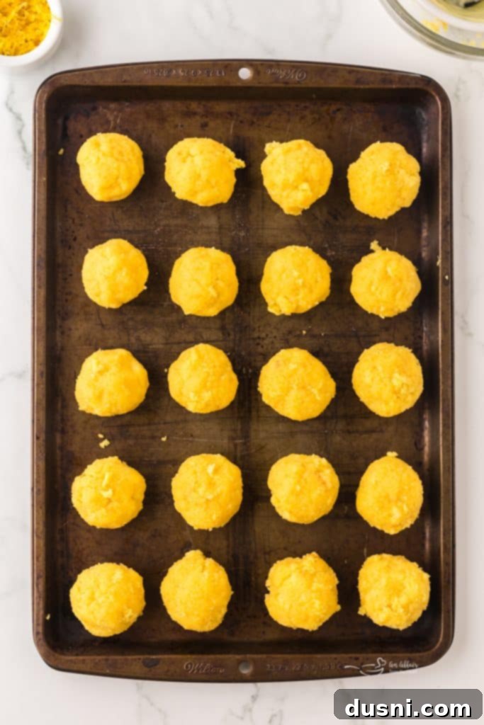 Hand rolling lemon cake mixture into balls on a baking sheet.
