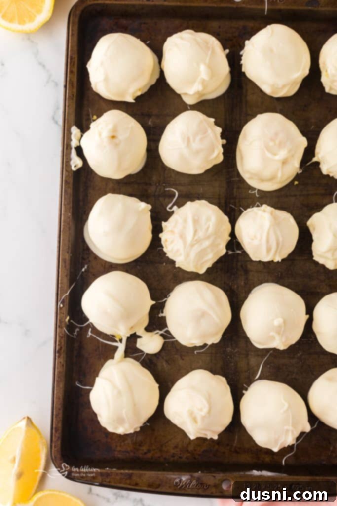 White chocolate lemon truffles cooling on a baking sheet, some with fresh zest.