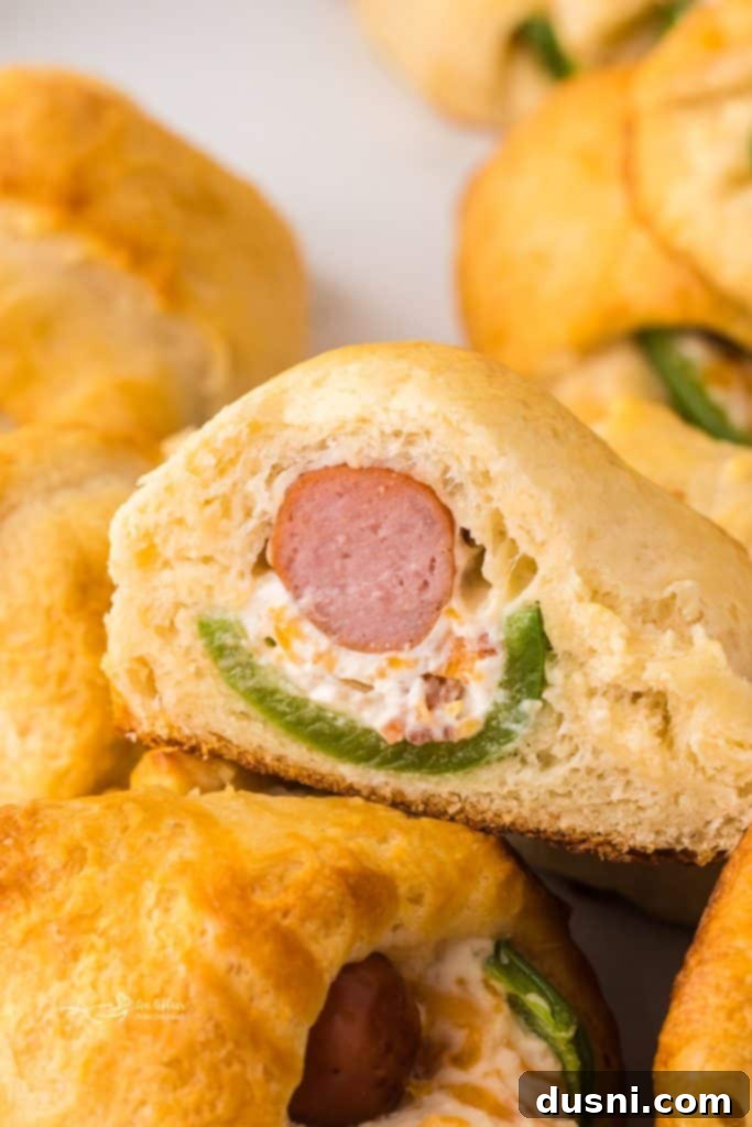 Stacked Jalapeño Popper Pigs in a Blanket on a platter, garnished with fresh jalapeño slices, ready to be served.