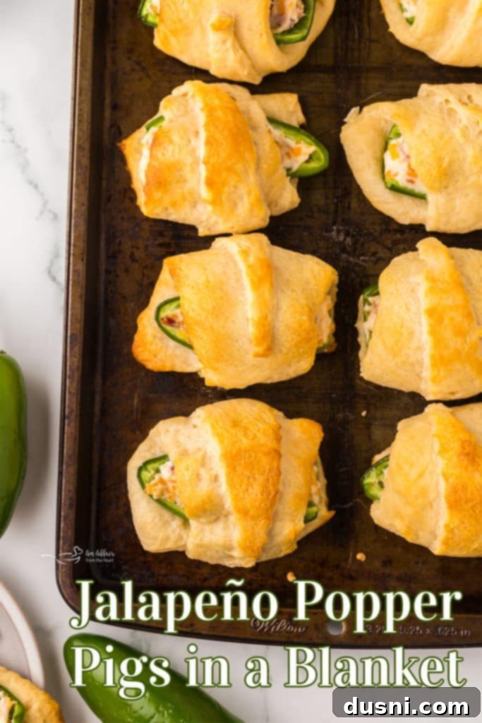 A large serving platter filled with numerous golden-brown Jalapeño Popper Pigs in a Blanket, garnished and ready to be enjoyed by guests.