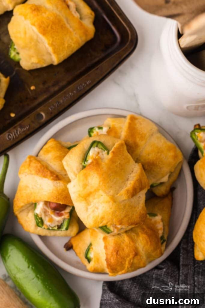 Close-up of a single Jalapeño Popper Pig in a Blanket, showing the golden-brown crescent roll and a hint of green jalapeño peeking out.