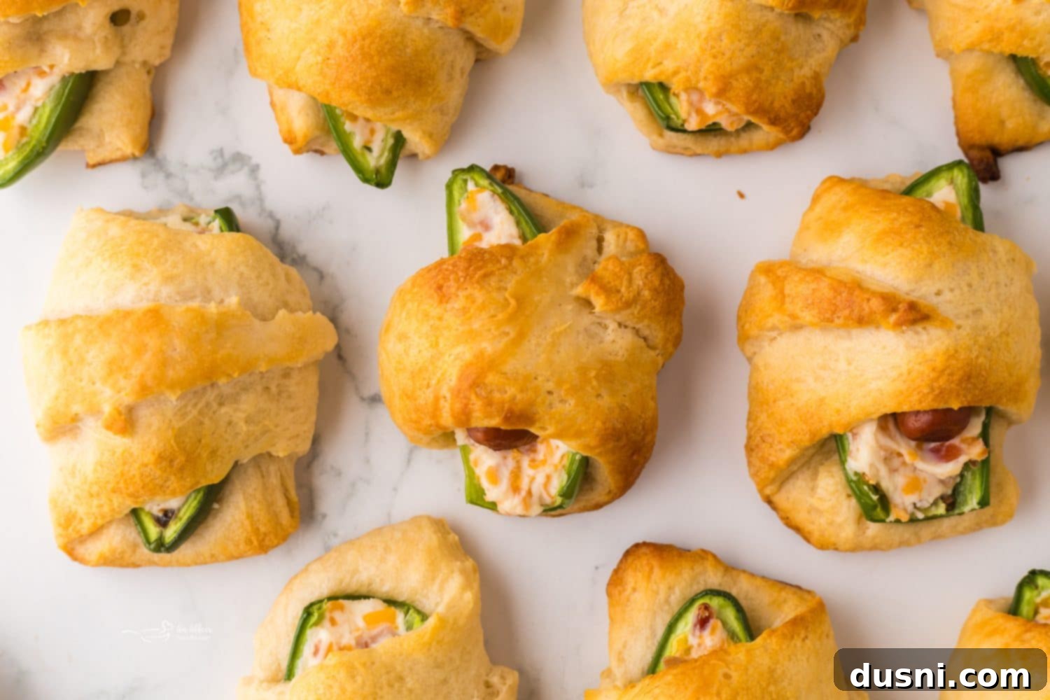 Several assembled Jalapeño Popper Pigs in a Blanket laid out on a baking sheet lined with parchment paper, ready to be baked.