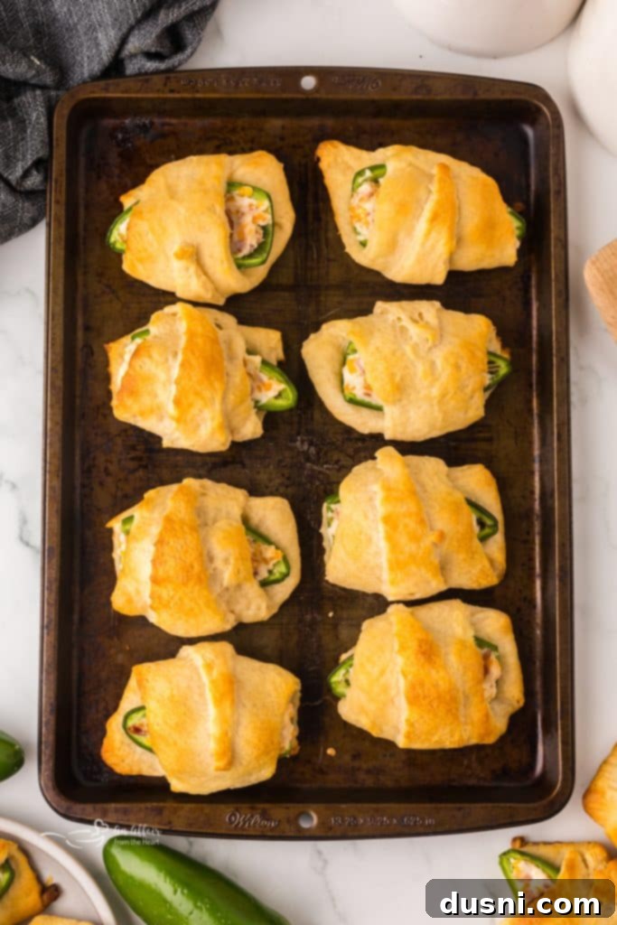 A close-up view of a Jalapeño Popper Pig in a Blanket being assembled: cream cheese-filled jalapeño with a mini sausage, ready to be wrapped in crescent dough.