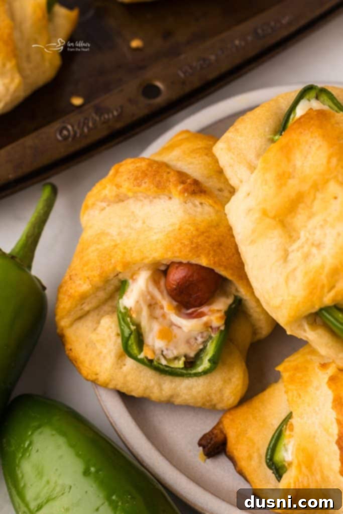 An appetizing close-up of a few Jalapeño Popper Pigs in a Blanket, showcasing the golden-brown pastry and creamy filling on a serving plate.