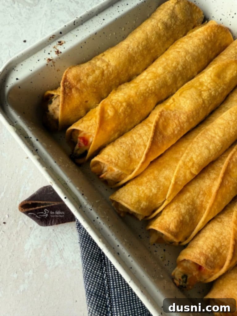 Taquitos arranged on a baking sheet, lightly brushed with olive oil, prepared for baking.