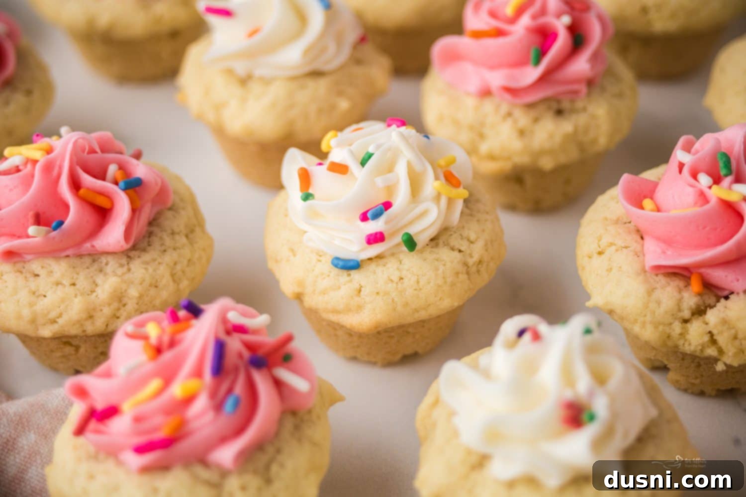 Delicious Frosted Sugar Cookie Cups 3 A tray of frosted sugar cookie cups with pink and white frosting and sprinkles.