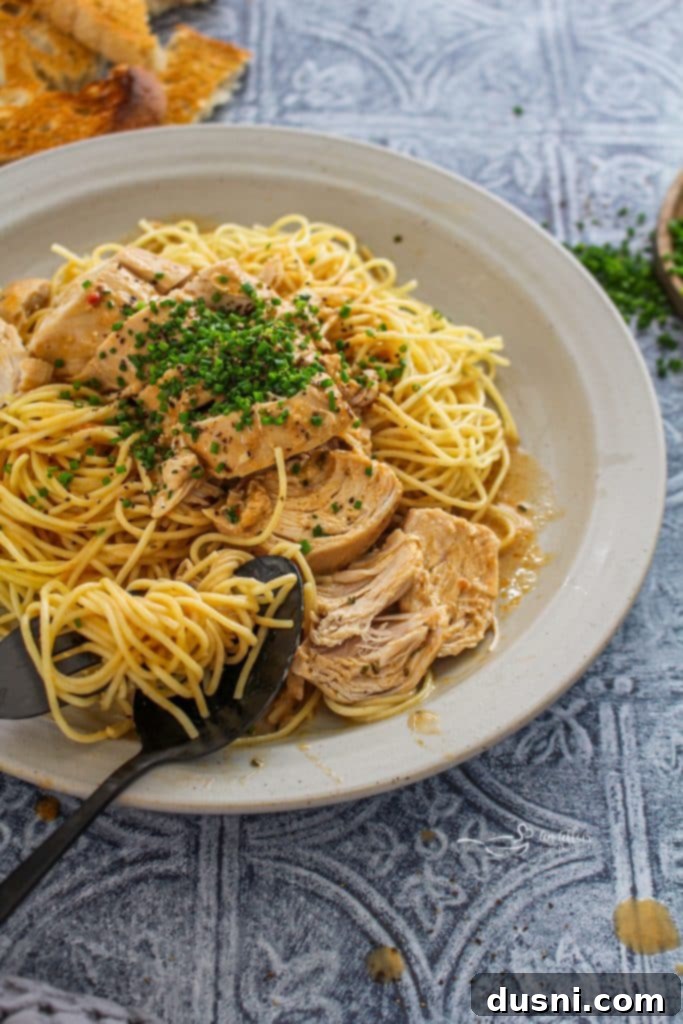 Slow Cooker Angel Chicken served over angel hair pasta, garnished with fresh chives.