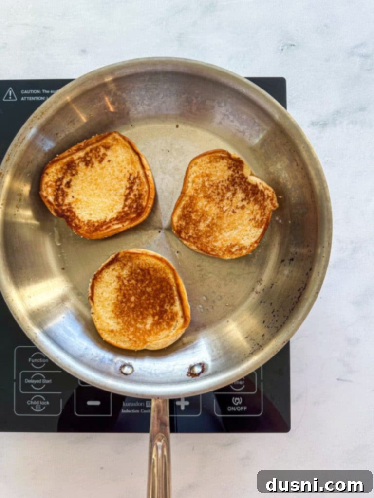 Sesame seed buns being toasted in a hot skillet with butter.