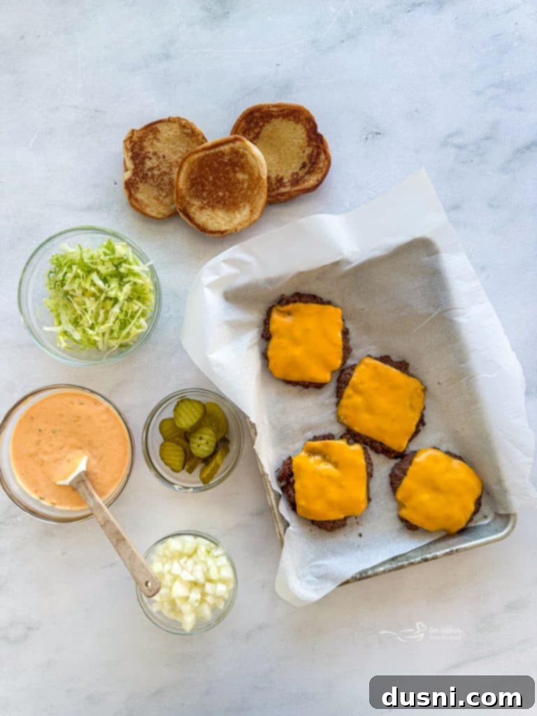 Thin burger patties cooking in a skillet, topped with American cheese slices melting.