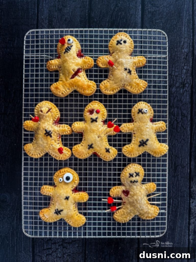 Mystic Doll Pastries 11 Two Voodoo Doll Hand Pies on a white background, one with a toothpick and icing, the other with visible cherry filling.
