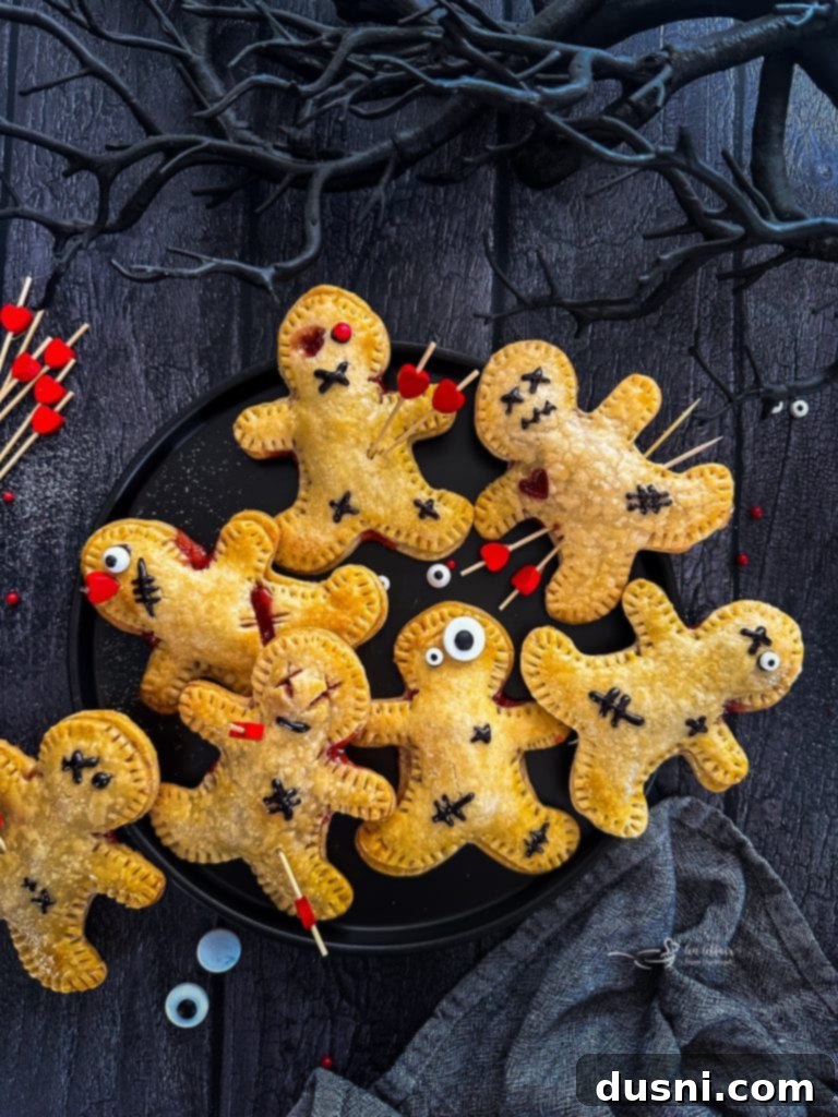 Mystic Doll Pastries 3 Close up of a Voodoo Doll Hand Pie, showing cherry filling oozing out, with black icing stitches and a toothpick pin.