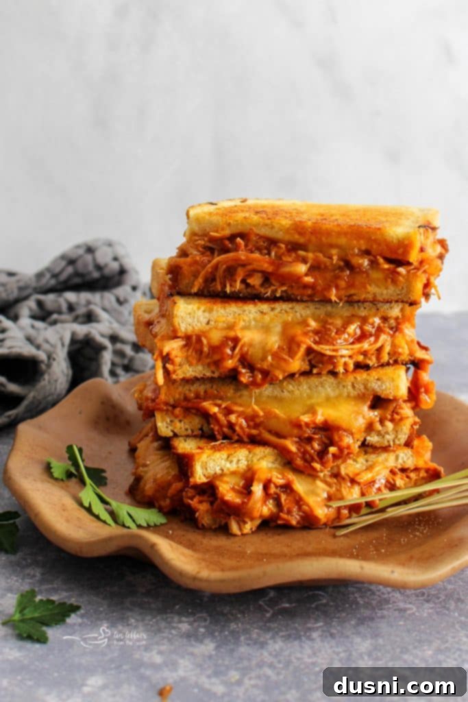 Close up of a BBQ Pulled Pork Grilled Cheese sandwich cut in half, showcasing melted cheese and shredded pork.