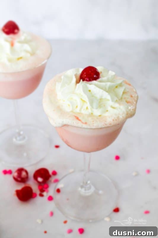 Velvet Almond Blush 13 Pink Squirrel cocktail in a stemmed glass with whipped cream and cherry.