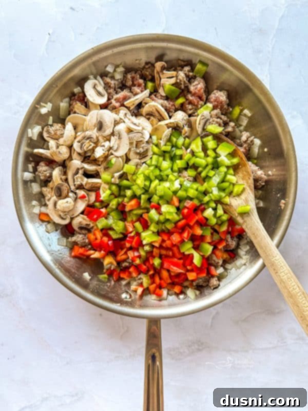 Adding mushrooms and bell peppers to the browning sausage