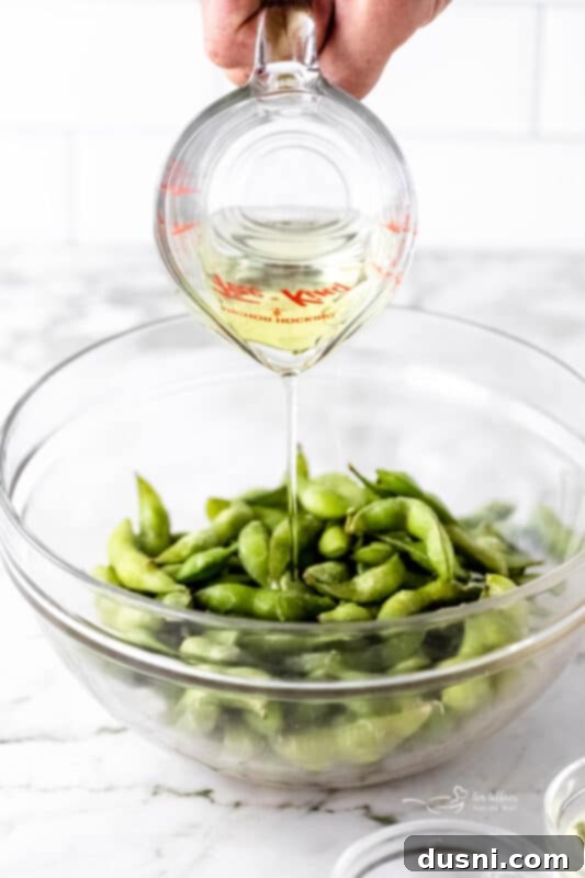 Edamame beans being mixed in a bowl with oil and salt