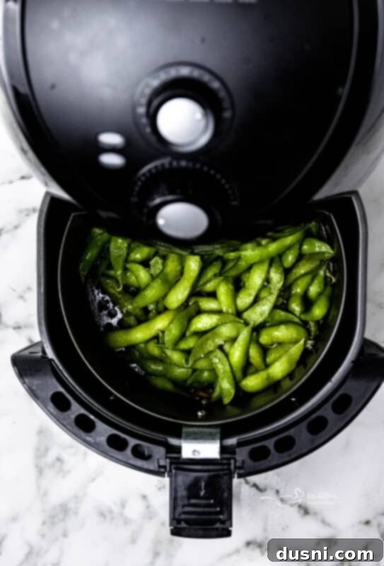 Air fryer basket being inserted with edamame beans