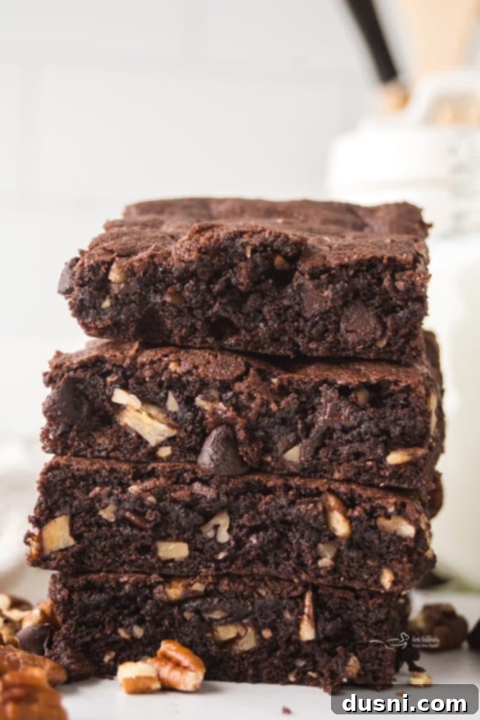A stack of three homemade pecan brownies on a white plate, showcasing their rich color and fudgy texture.